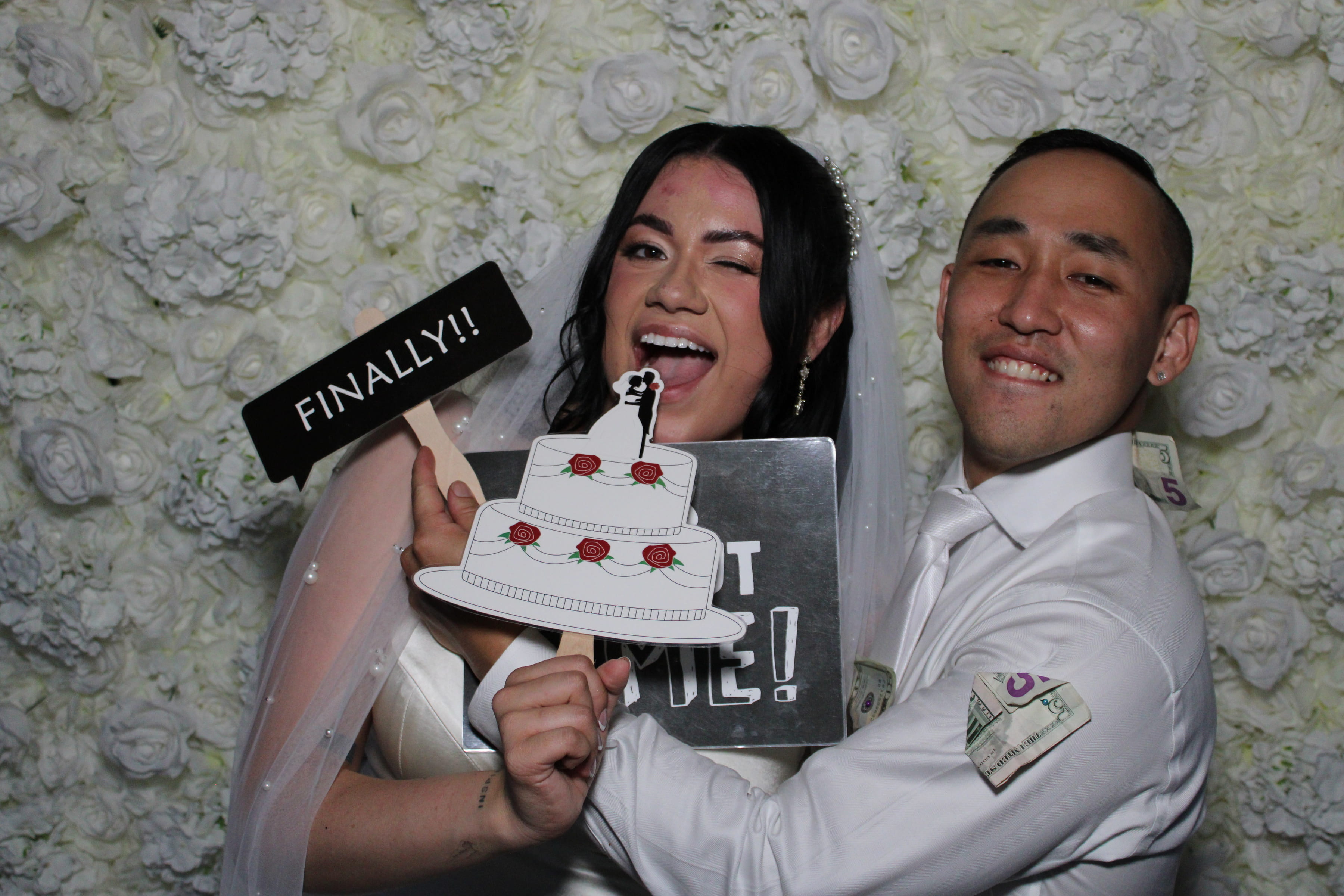 Bride and groom celebrating in the Pixy Shots Selfie Booth — white floral backdrop, 'Finally!!' photo prop